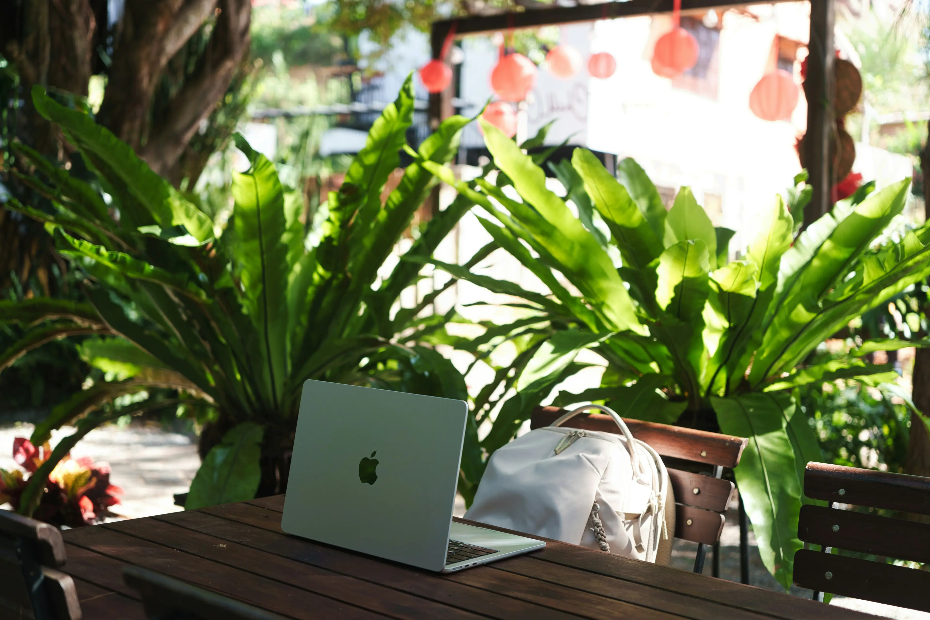 A laptop on a wooden table in a leafy café garden